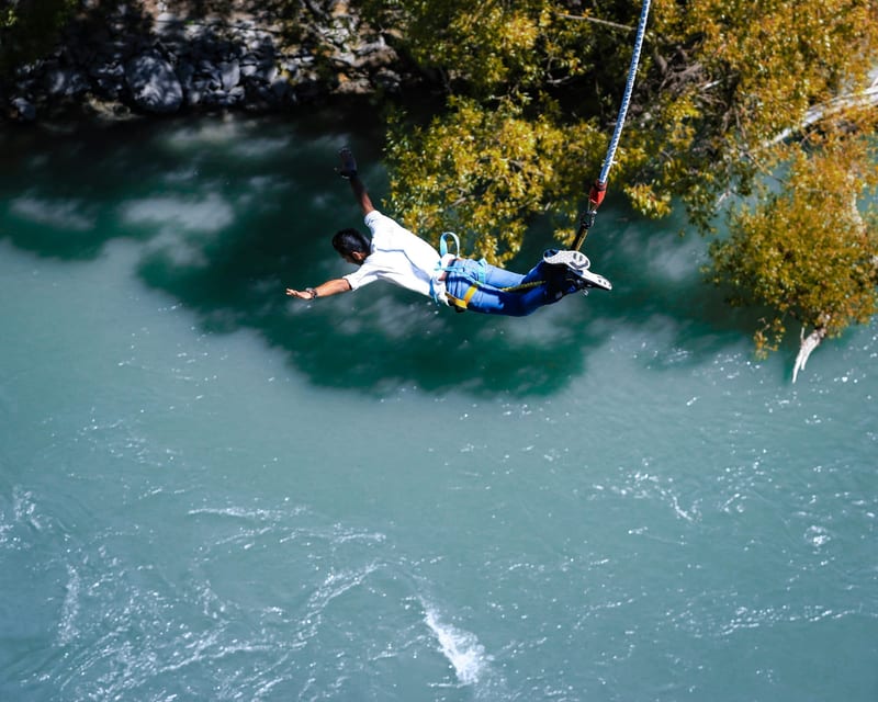 A bungee jumper freefalling head-first toward a turquoise river