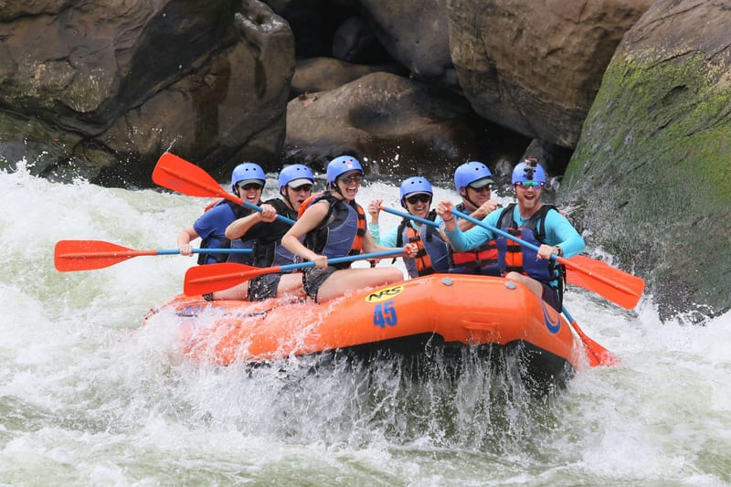 A group of six whitewater rafters paddling through rapids in an orange raft