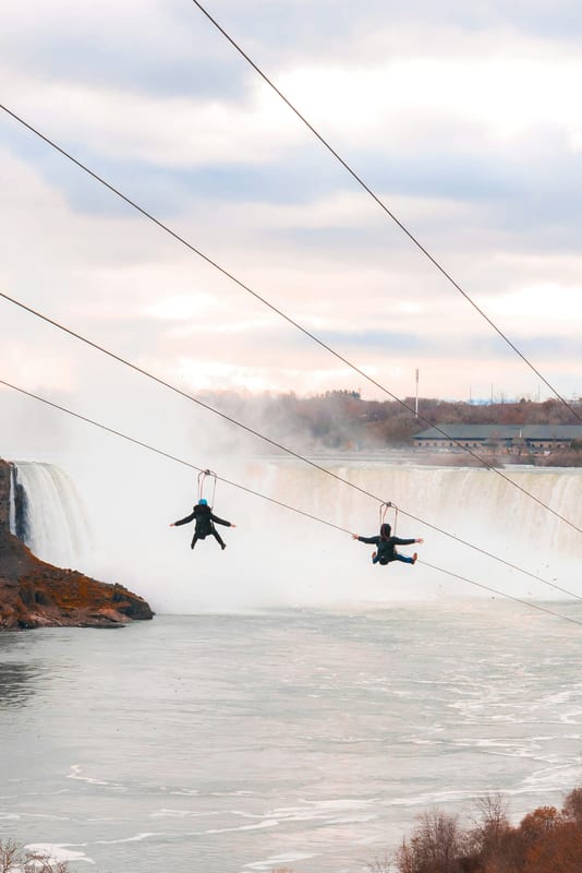 Two zipliners riding the WildPlay MistRider zipline toward Niagara Falls